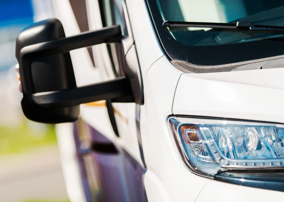 A close-up of a white van with headlights and wing mirror prominent.